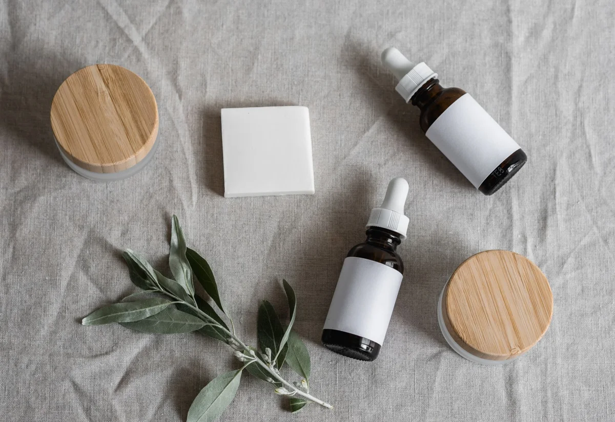 Frascos de sérum y tarros de crema sobre lino junto a una rama de olivo