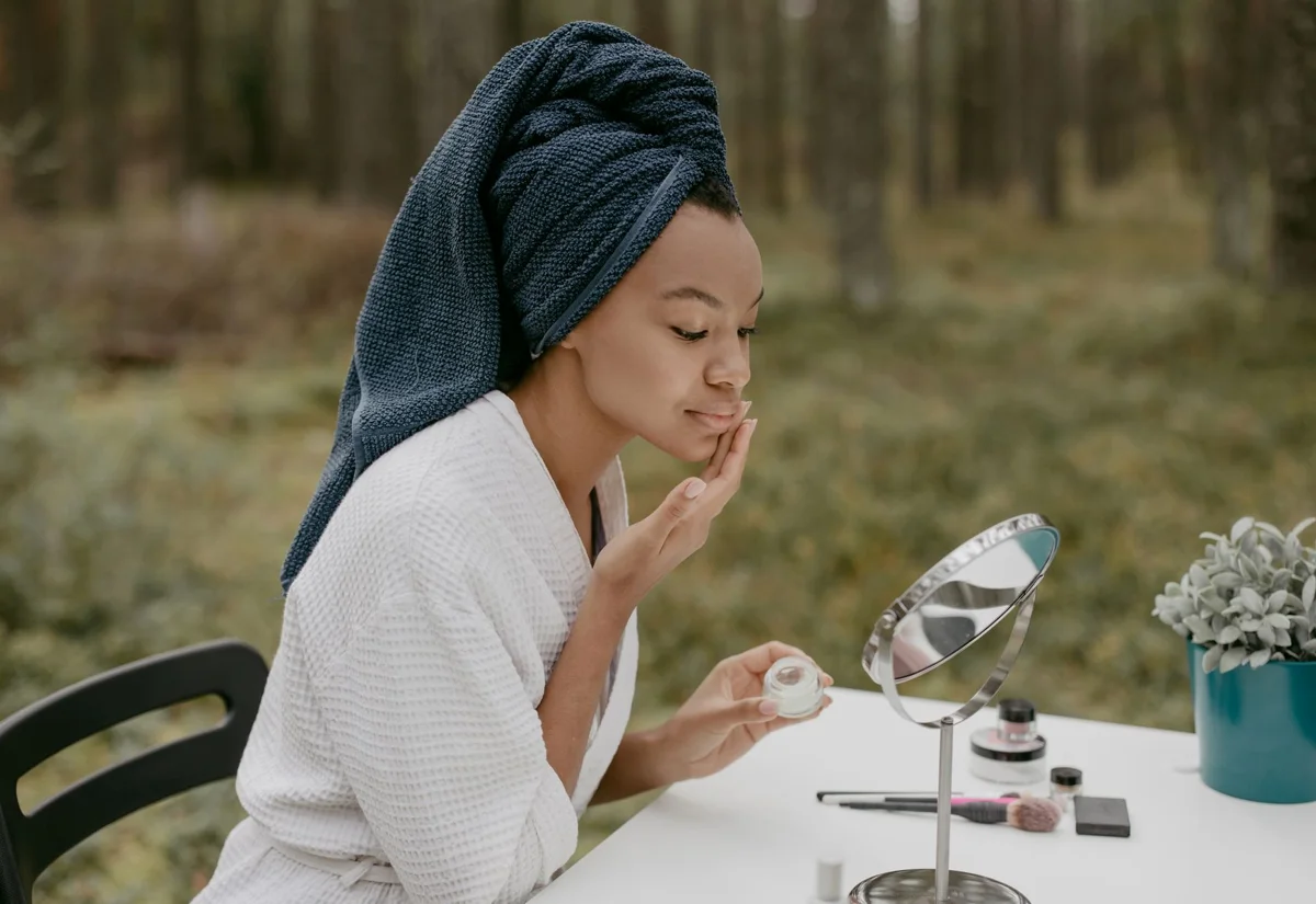 Mujer aplicándose crema facial con calma al aire libre, junto a un bosque